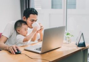 Asian little son helping father drinking coffee between working with laptop computer notebook at workplace happy family together at home concept.